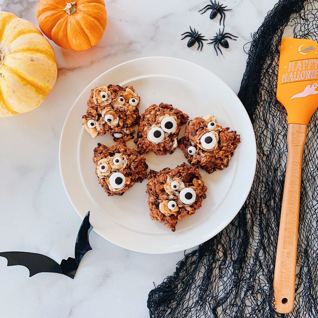 A plate of Halloween themed monster cookies with googly eyes in spooky setting.
